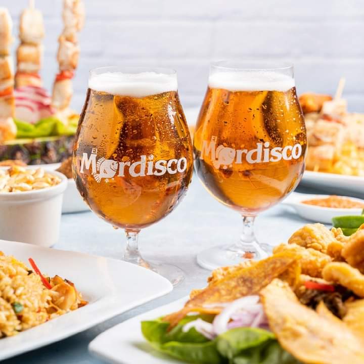 Dos copas con el logo de El Mordisco, rodeadas de distintas fuentes de pescados y mariscos.